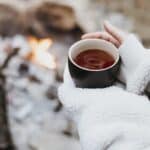 Person holding a warm cup of hot chocolate in the snow, reflecting and finding comfort during winter.