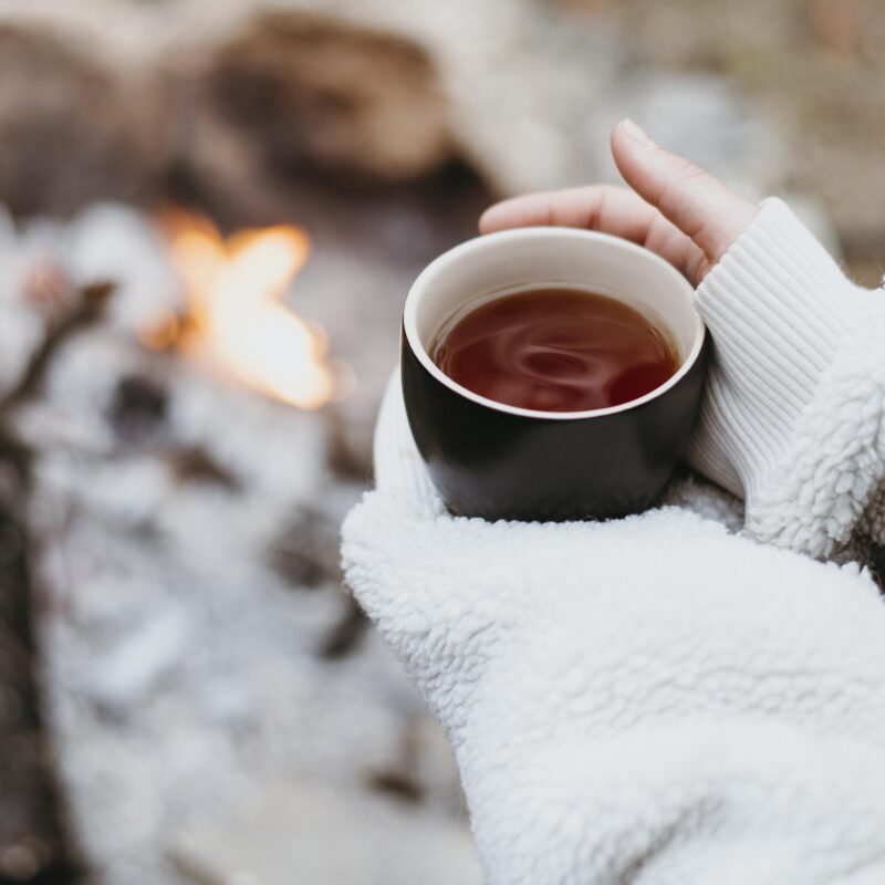 Person holding a warm cup of hot chocolate in the snow, reflecting and finding comfort during winter.