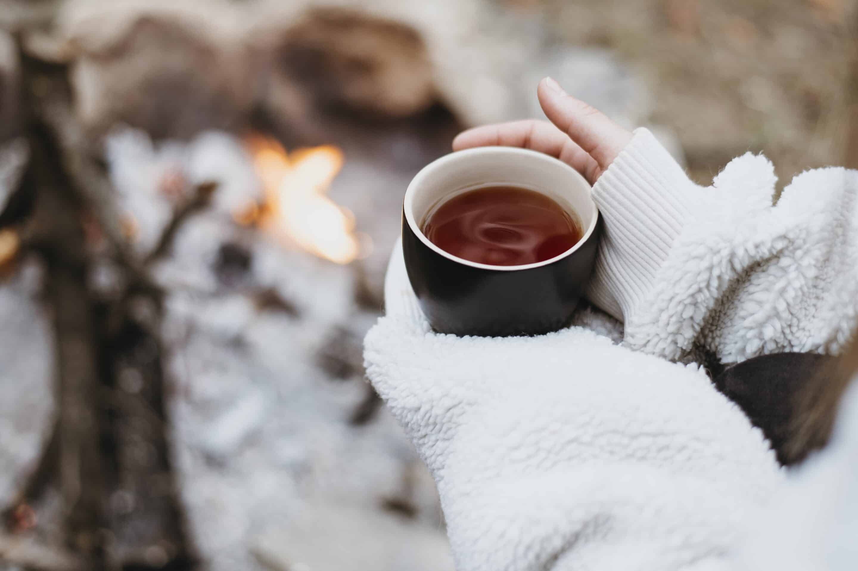 Person holding a warm cup of hot chocolate in the snow, reflecting and finding comfort during winter.